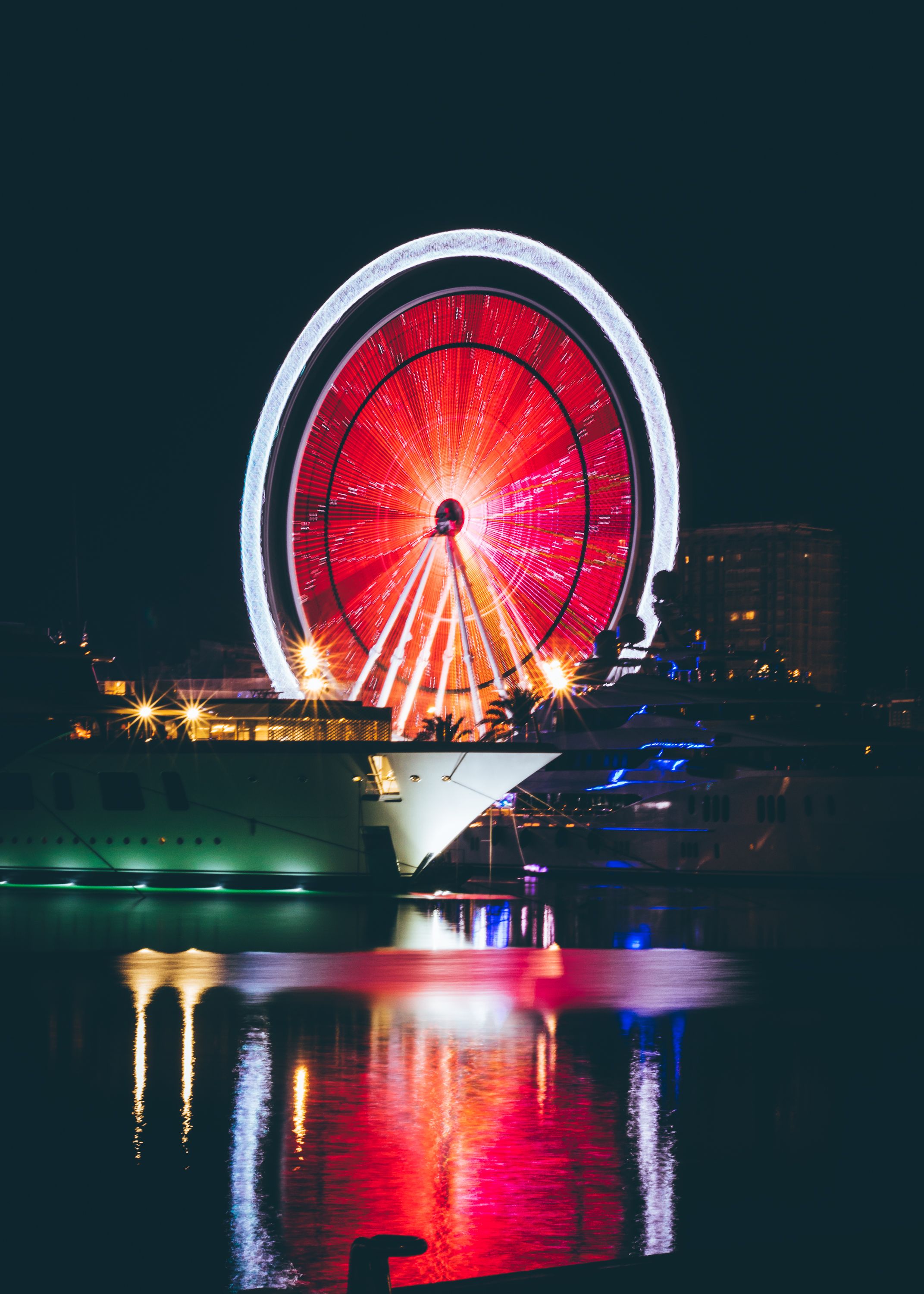 主题公园的水面上，一个照明的摩天轮倒映出五颜六色的光影，夜景令人惊叹