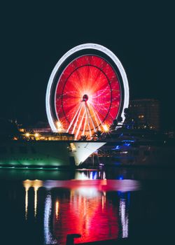 主题公园的水面上，一个照明的摩天轮倒映出五颜六色的光影，夜景令人惊叹