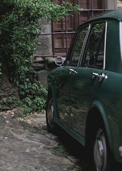一辆经典的绿色汽车停在绿色的石头建筑旁边