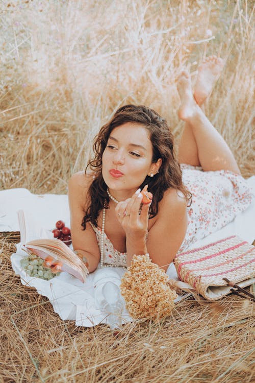 Smiling Woman Lying Down on Picnic Blanket and Eating