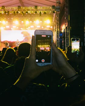 A person records a vibrant concert scene on their smartphone amidst a lively crowd.