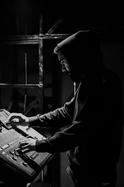 Free A man in a hoodie stands in dim lighting, operating a control panel. Stock Photo