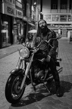 Black and white image of a man sitting on a motorcycle in a city street at night.