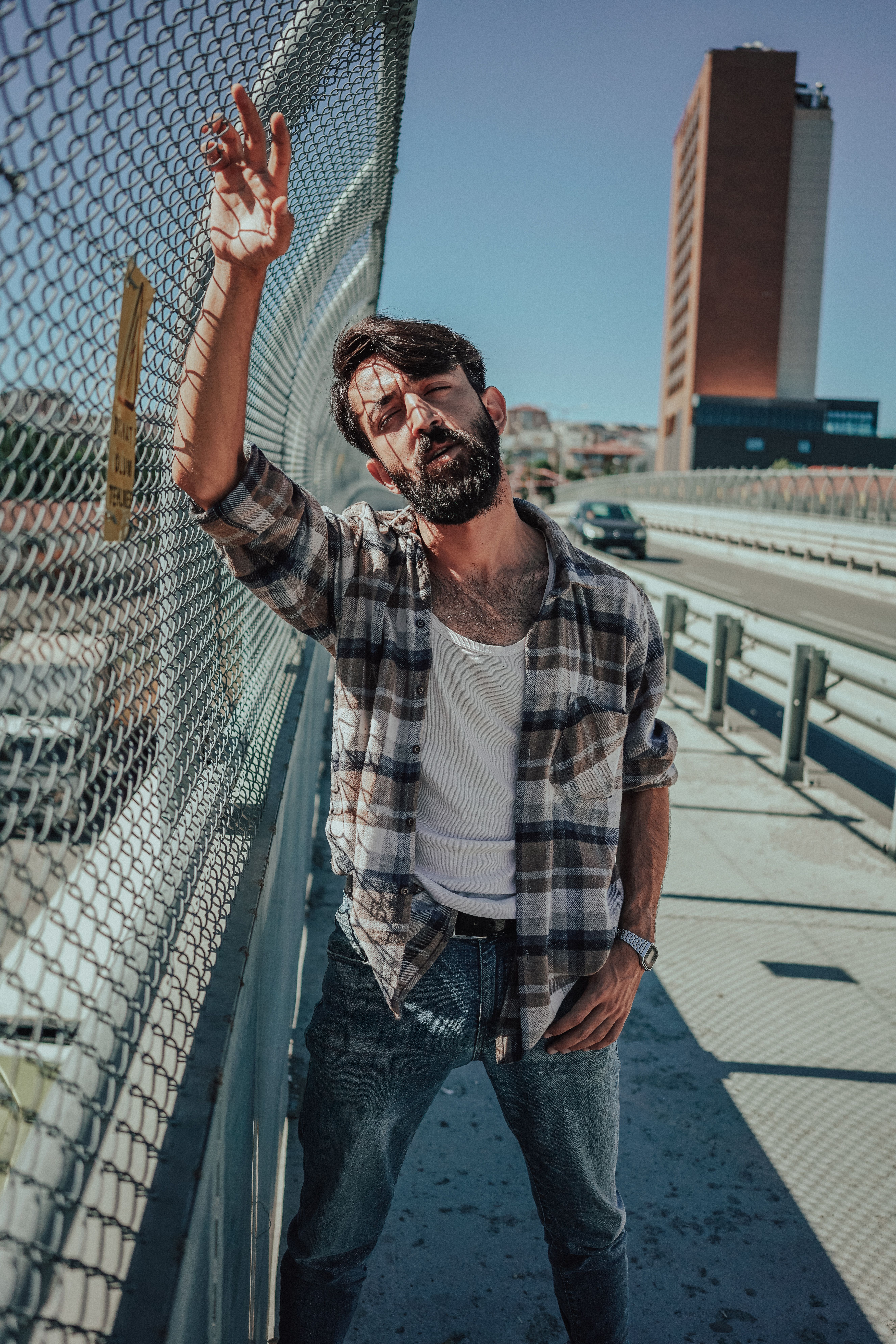 A man in a flannel shirt poses confidently outdoors, showcasing urban fashion.