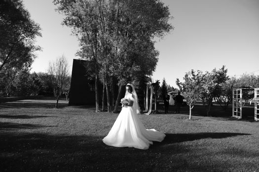 A bride in a wedding dress stands gracefully in a garden, captured in black and white.