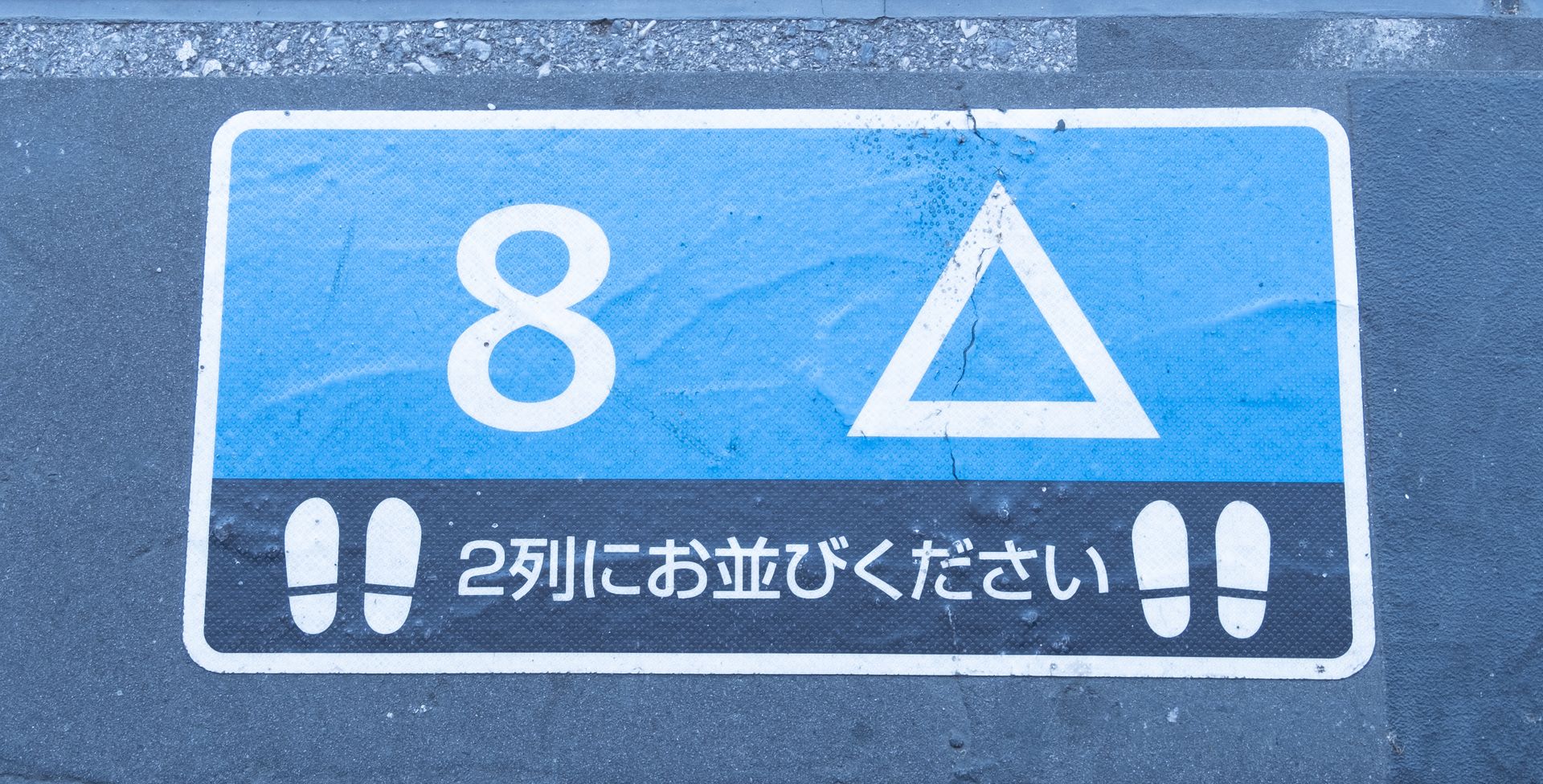 Blue and white queue sign with numbers and symbols on pavement in Japan.