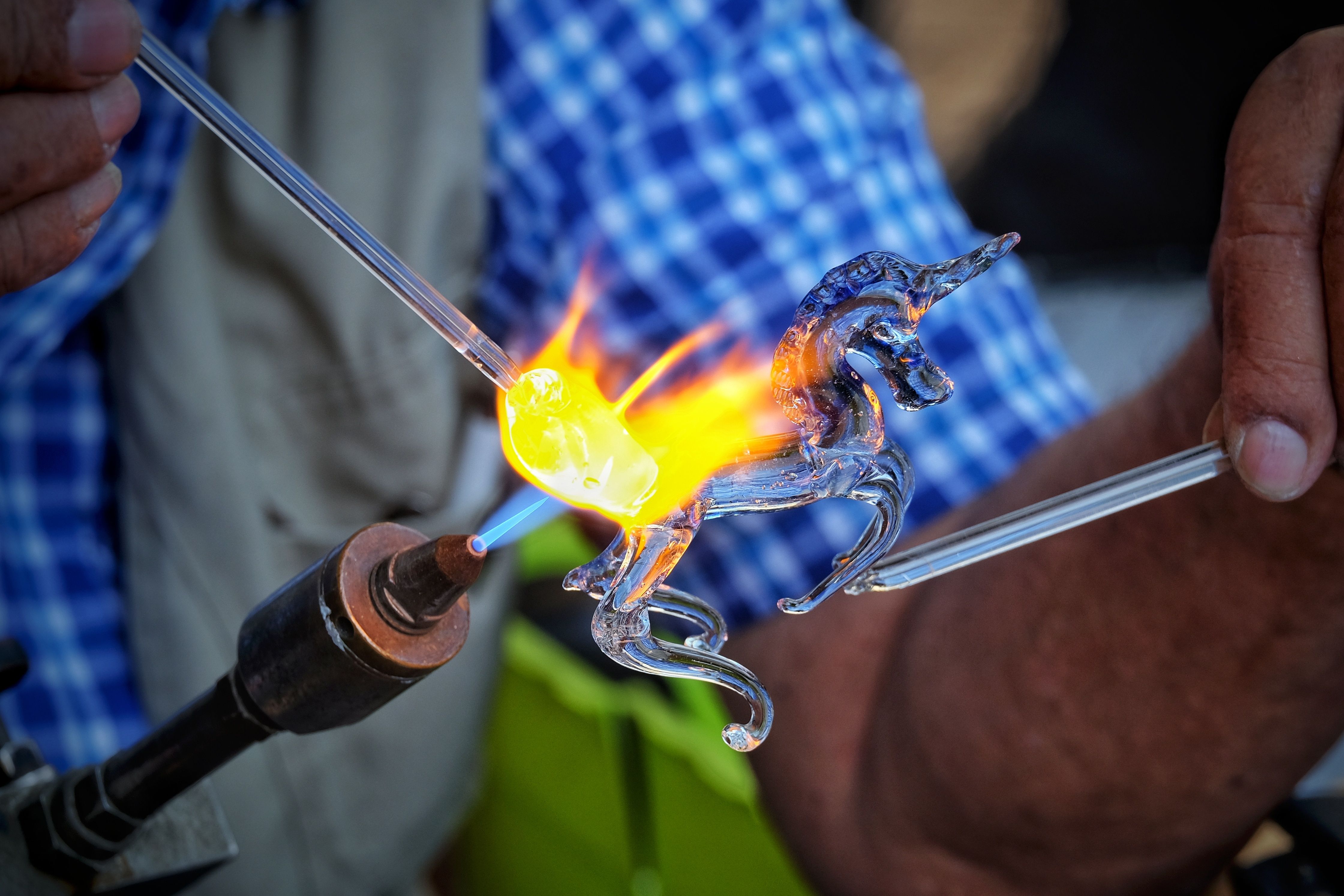 A glass figure being shaped in a torch flame at the bench