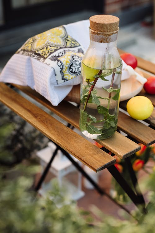 A Glass of Water with Lemon and Mint Standing on a Table Outside 