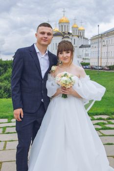 Charming couple in wedding attire posing with a historic church. Perfect for wedding photography collections.