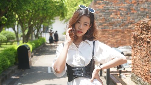 Free Fashionable brunette posing on a sunny day in an urban outdoor setting with greenery. Stock Photo