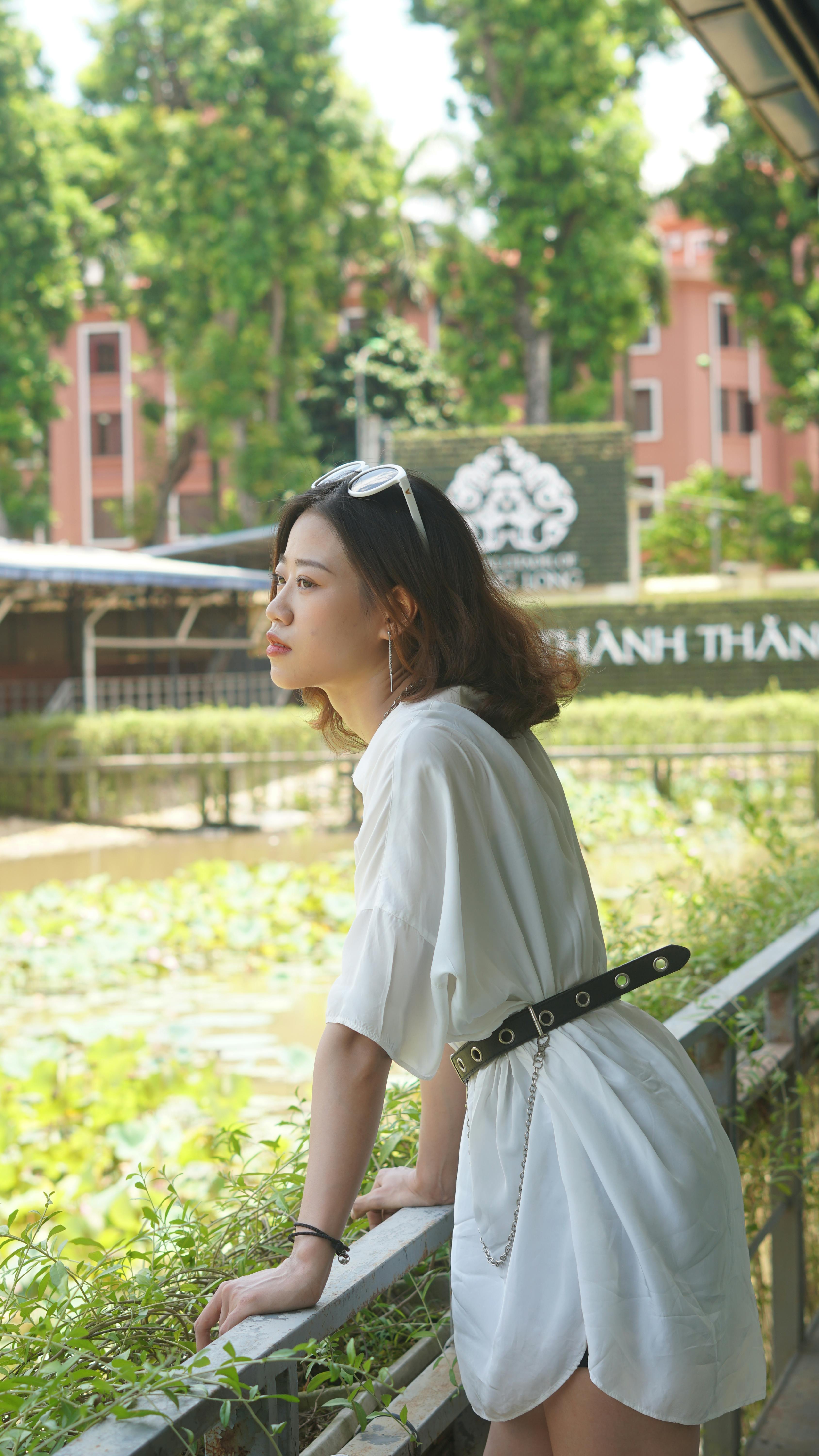 Elegant young woman in white attire enjoying a summer day outdoors by the railing.