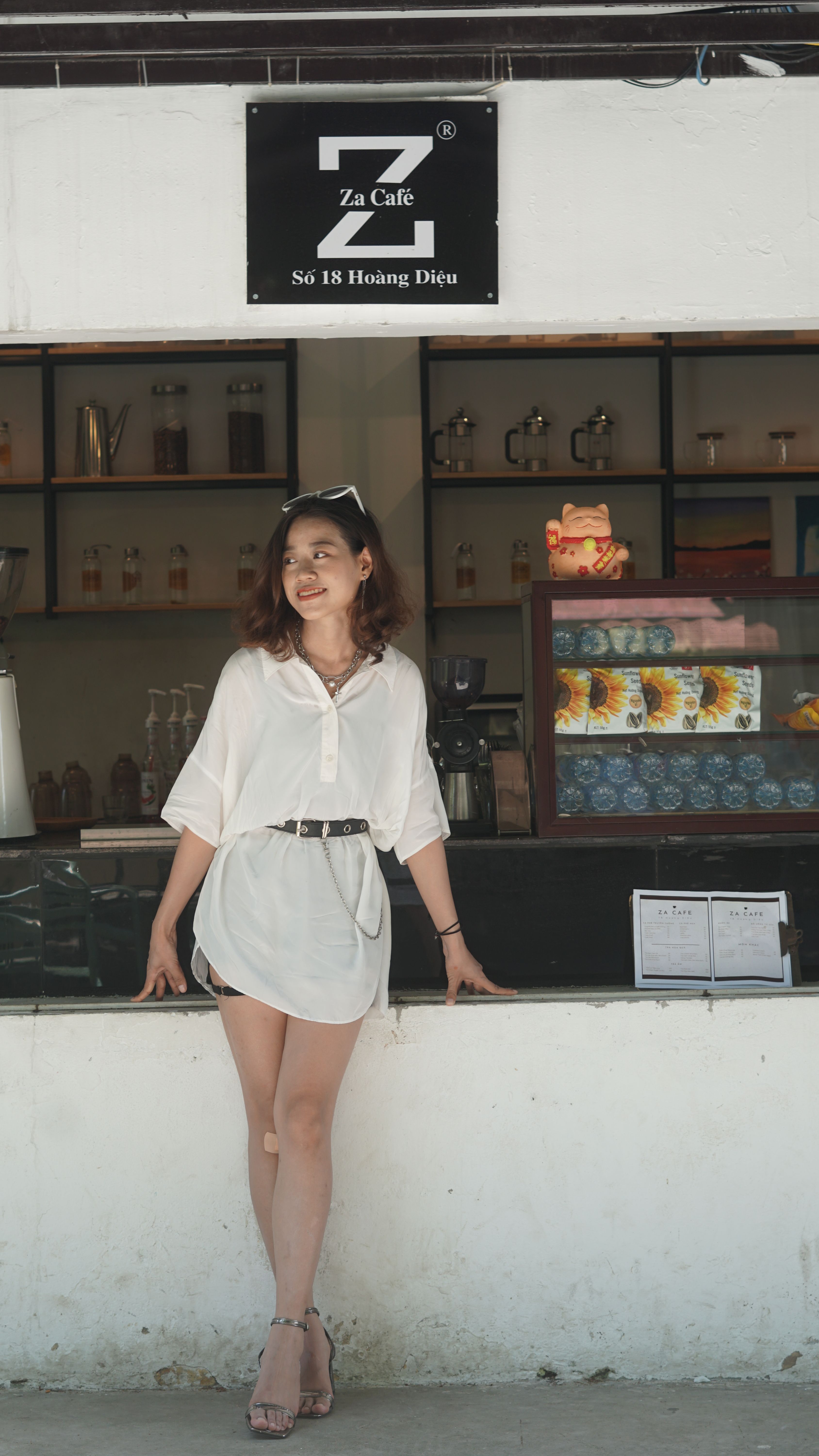 Young woman in fashionable outfit smiling at outdoor café on a sunny day.
