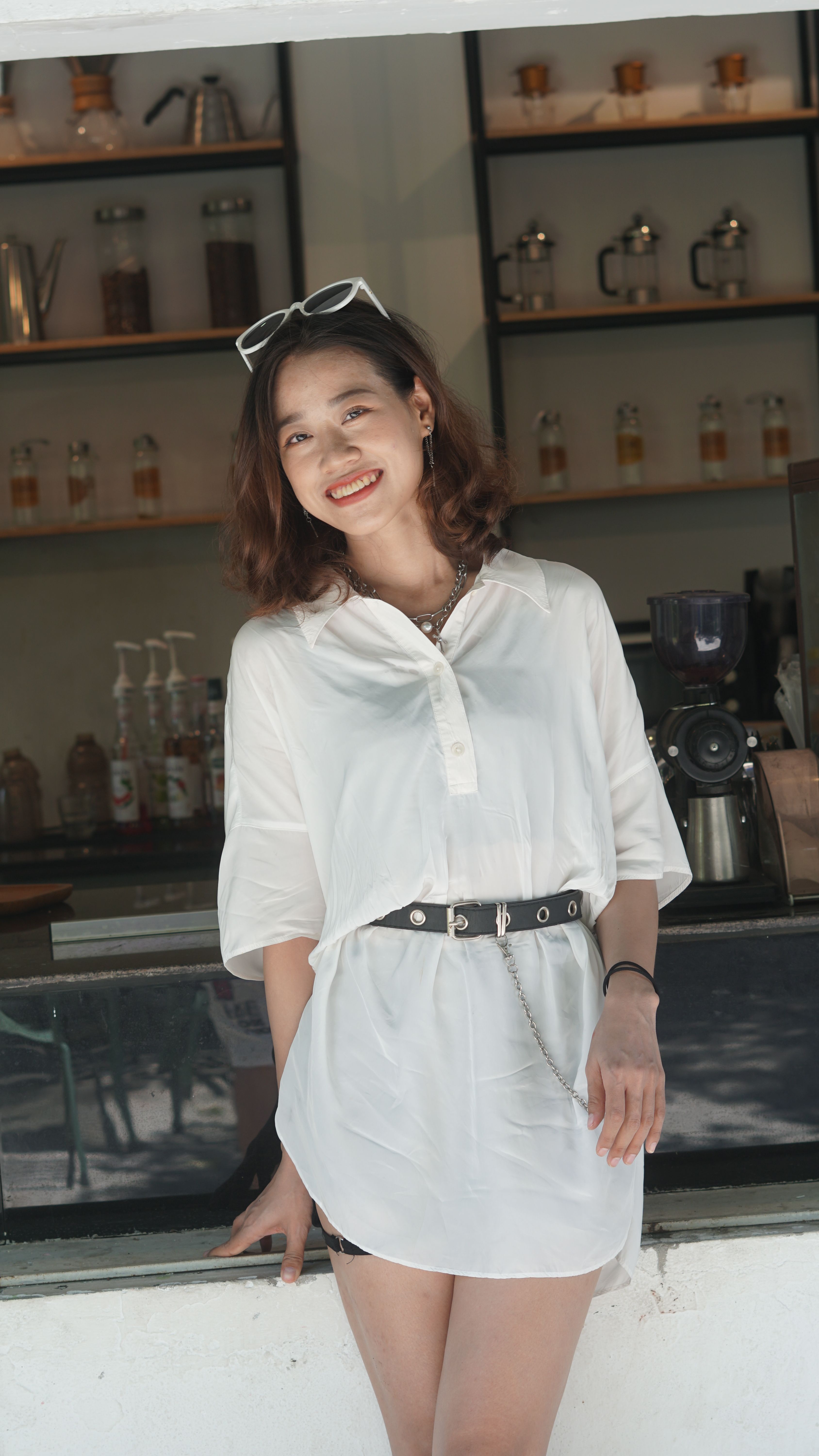 A fashionable young woman poses in a white outfit at a café counter, exuding summer vibes.