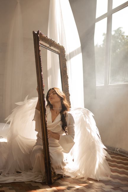 Artistic portrait of a woman with angel wings in a sunlit room, capturing divine beauty and tranquility.