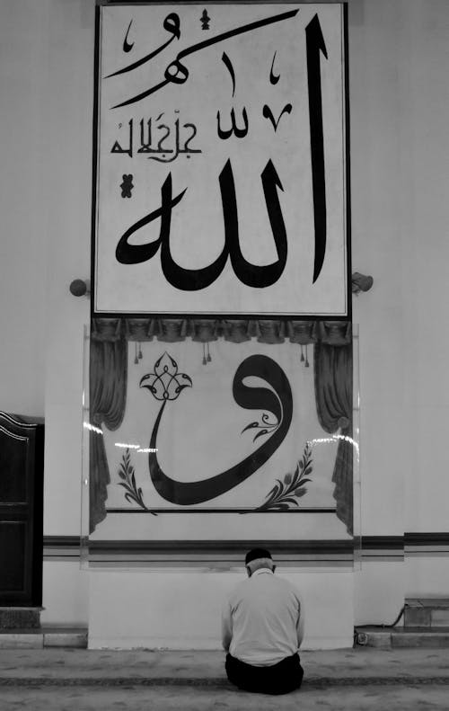 A Man Sitting in Front of a Banner with Arabic Script