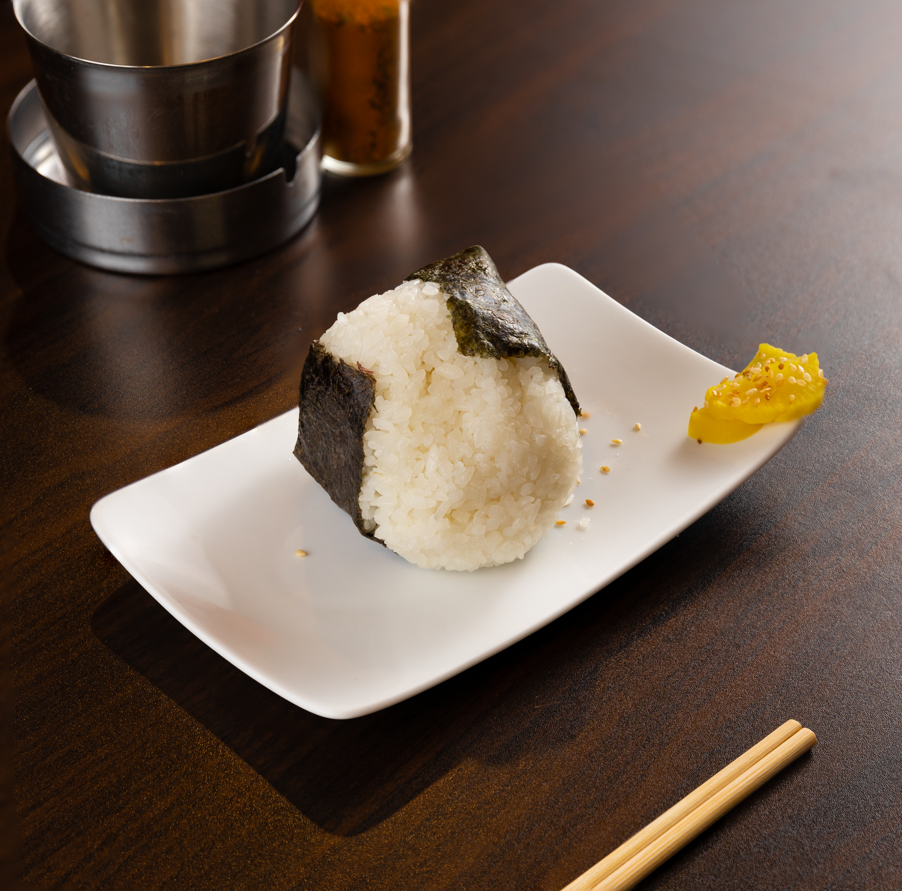 A scrumptious onigiri wrapped in nori, beautifully plated with a pickle on a dining table.