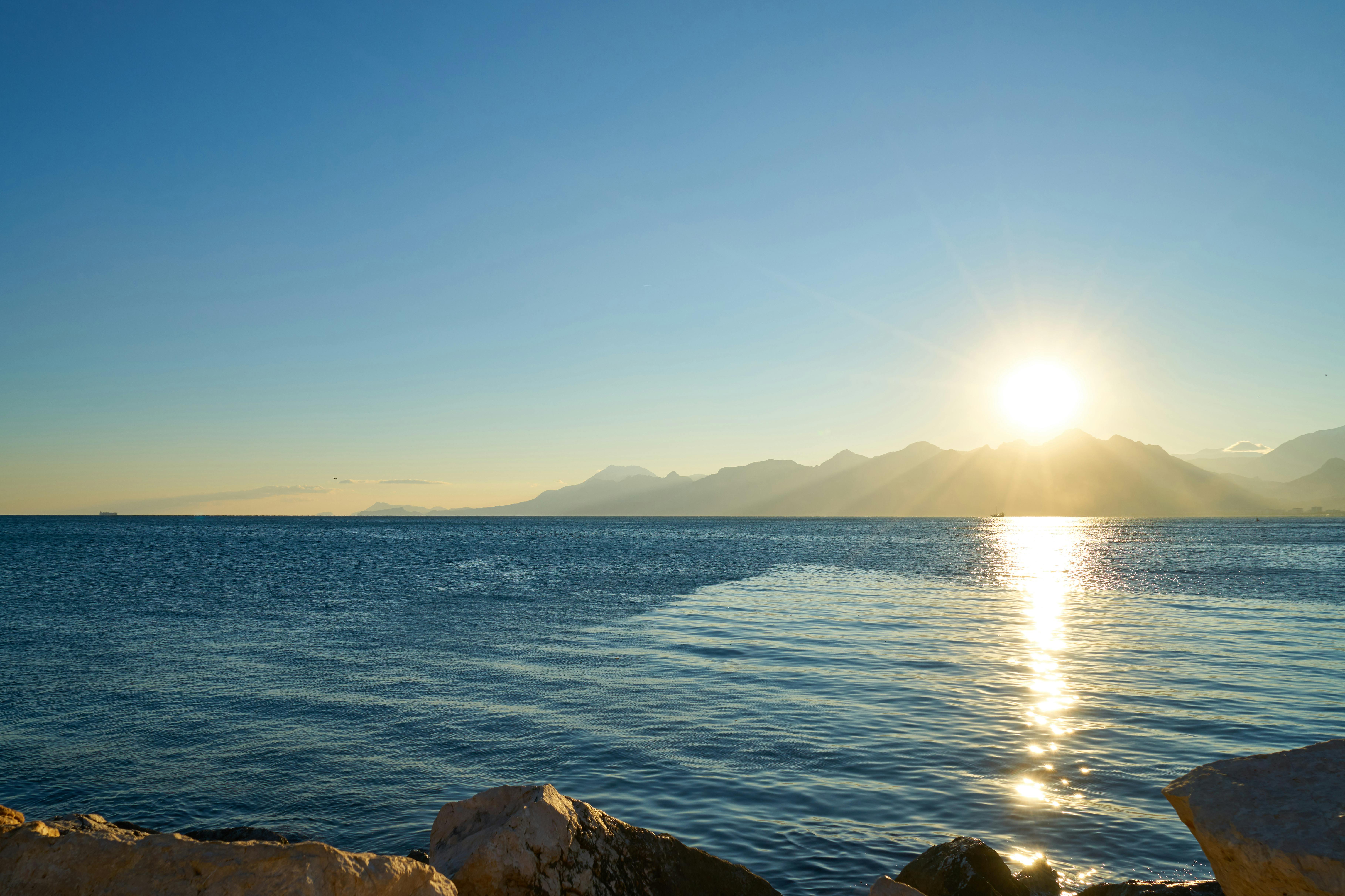 宁静的日出映照在多山的海景上，海水湛蓝清澈，倒影宁静