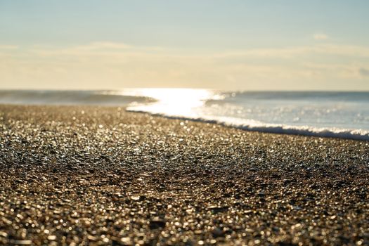 A serene pebble beach glistening in the sunlight, surrounded by calm ocean waves.