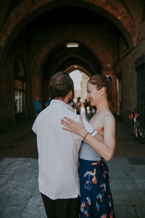 Free Couple embraces tenderly under a historic archway in urban setting, capturing a moment of connection. Stock Photo