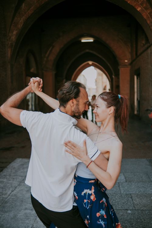 Free A joyful couple dancing under historic arches in an old town setting, reflecting happiness. Stock Photo