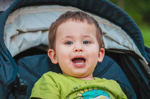 Free Smiling toddler in a stroller enjoying a sunny day outdoors, displaying innocence and joy. Stock Photo