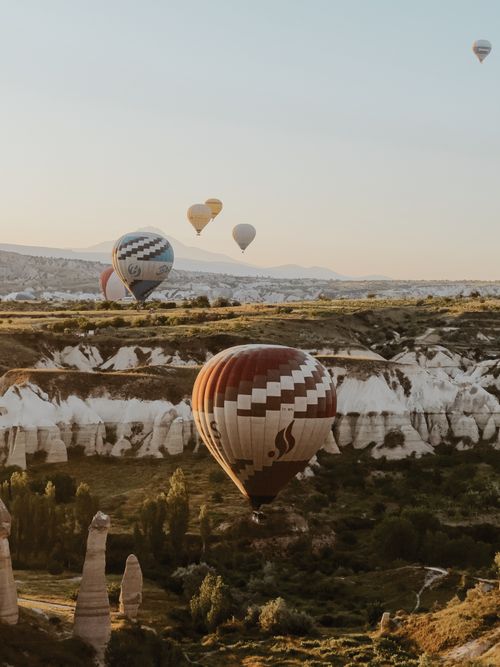 Free Scenic view of hot air balloons soaring over Cappadocia's rocky landscape at sunrise. Stock Photo