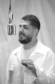 A male musician singing in a studio, eyes closed, white shirt.