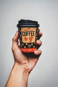 Close-up of a hand holding a stylish coffee to go cup against a neutral background.