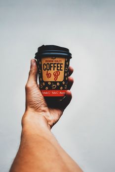 Close-up of a hand holding a coffee to-go cup against a white background in Mérida, Venezuela.