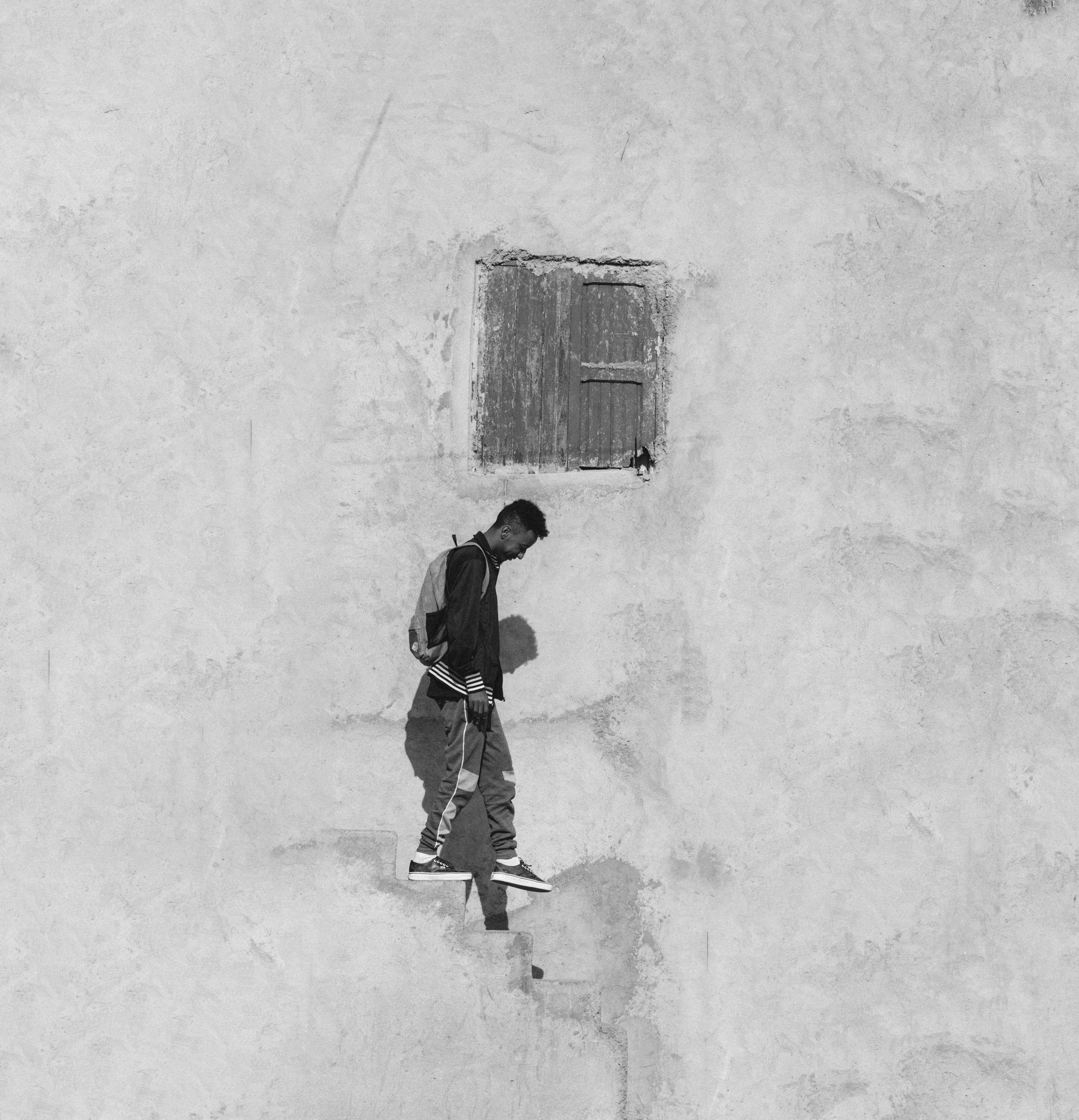 Black and white photo of a man walking down stairs against a textured wall.