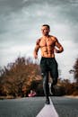 一个光着膀子的男人在铺满秋叶的道路上慢跑，展现着健身与户外运动的活力