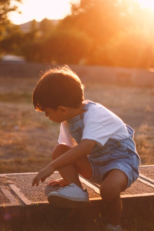 Free Young boy in denim overalls playing outside at sunset, with a soft golden lens flare. Stock Photo