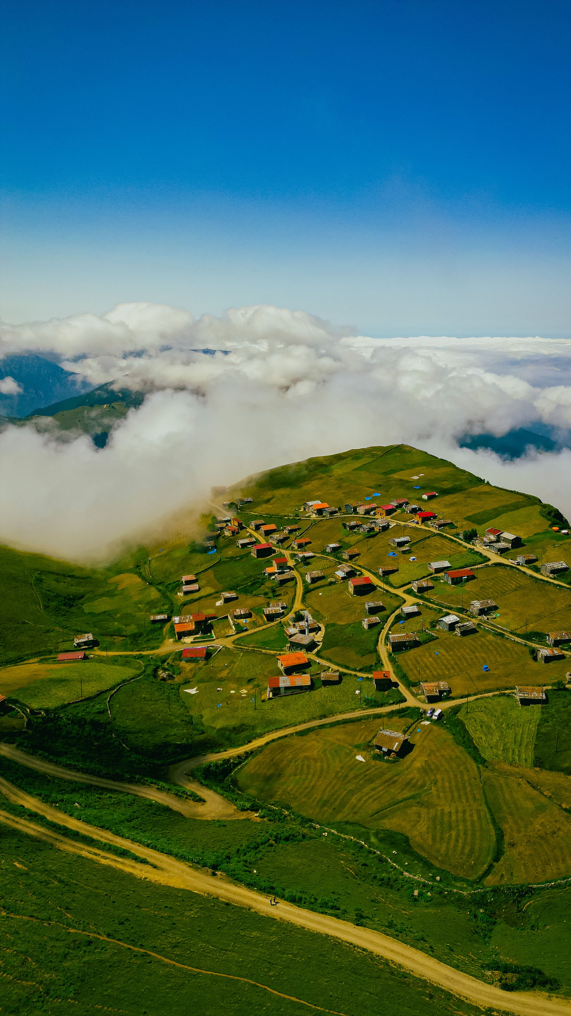 Stunning aerial view of a sunlit mountain village on a lush green plateau surrounded by clouds.