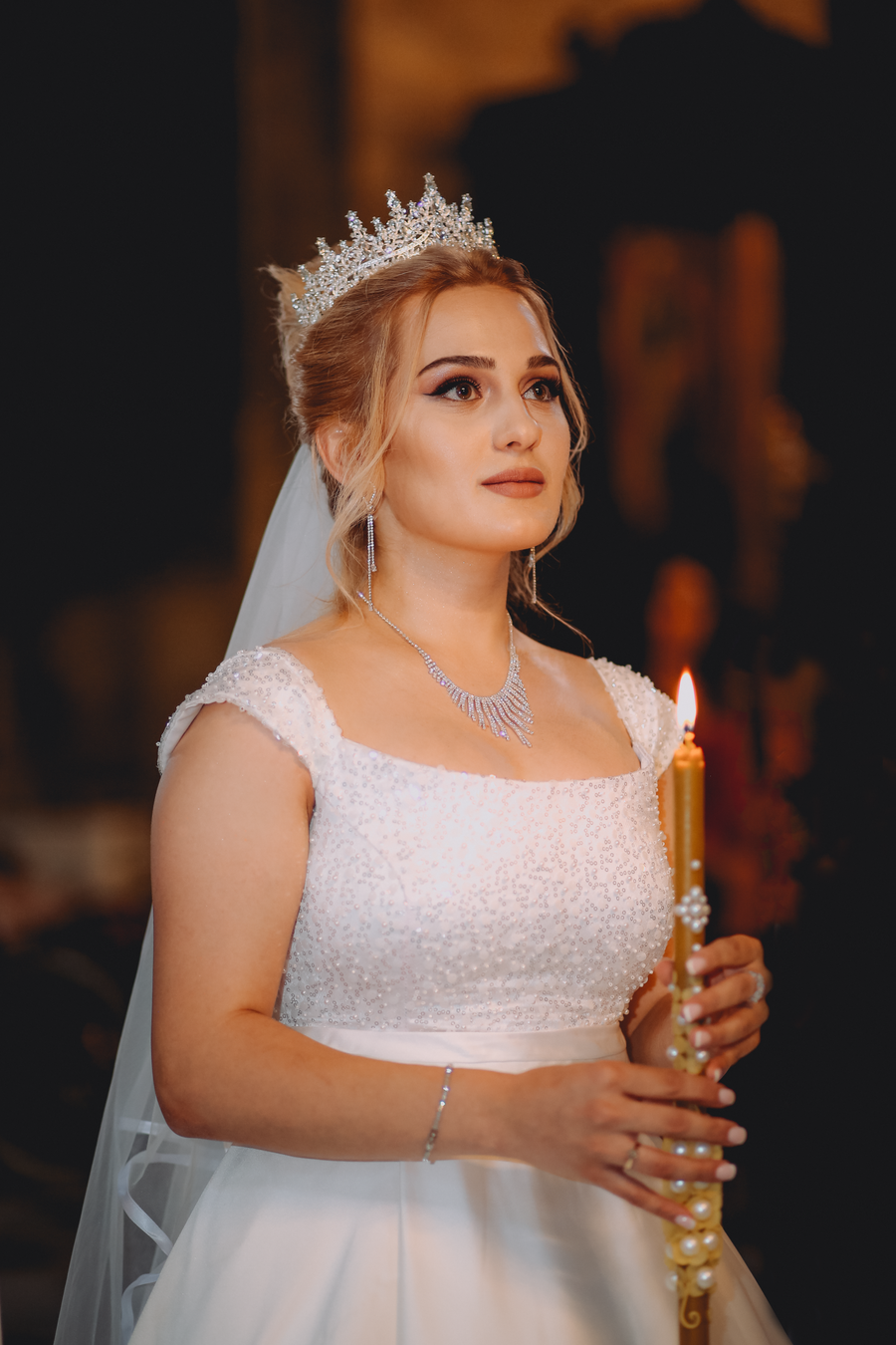 Bride in a white dress with a tiara holding a candle