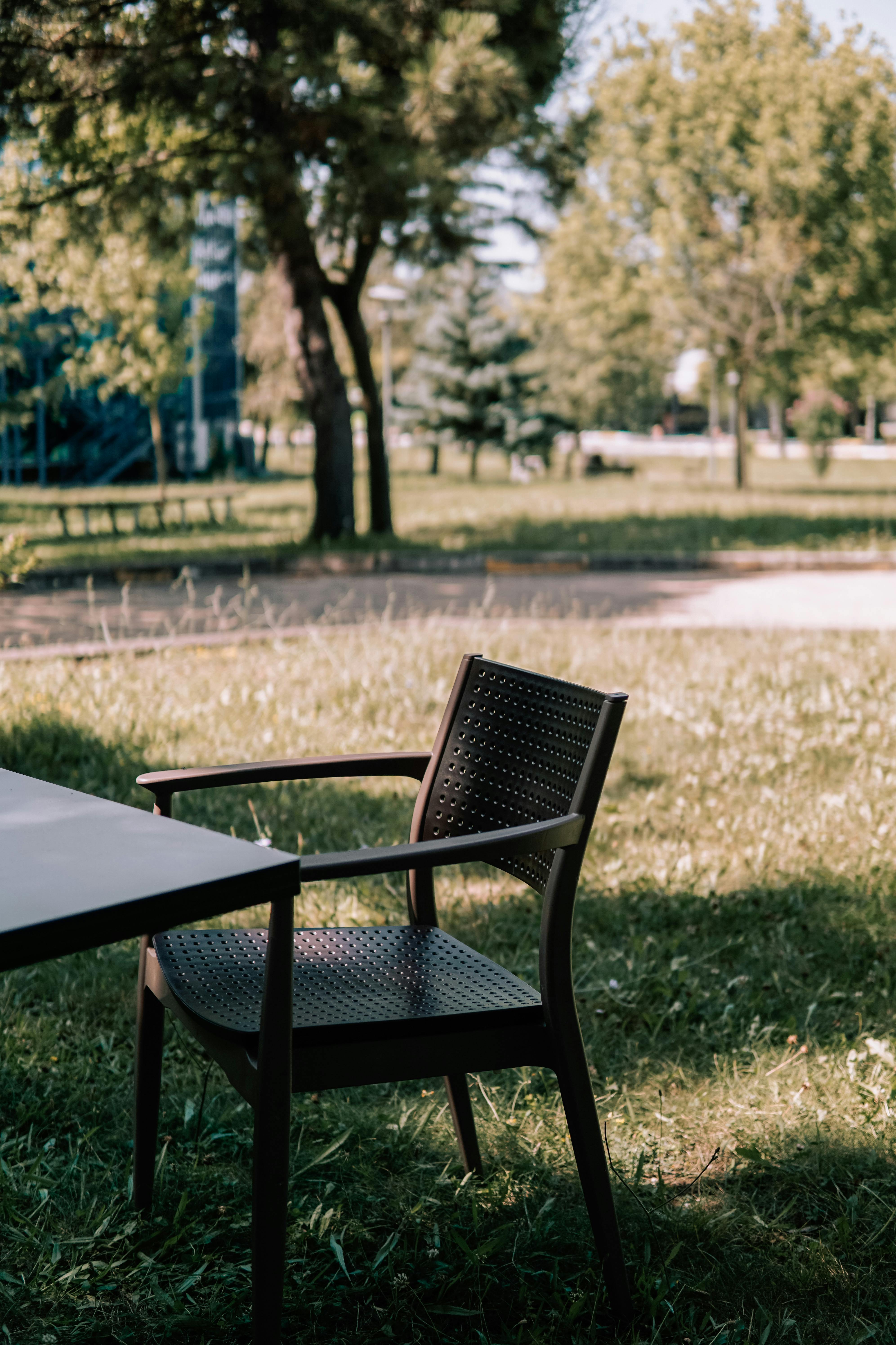 A solitary chair by a table in a tranquil sunlit park, surrounded by green grass.
