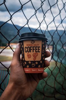 Hand holding a coffee to go cup with mountains in background, Mérida, Venezuela