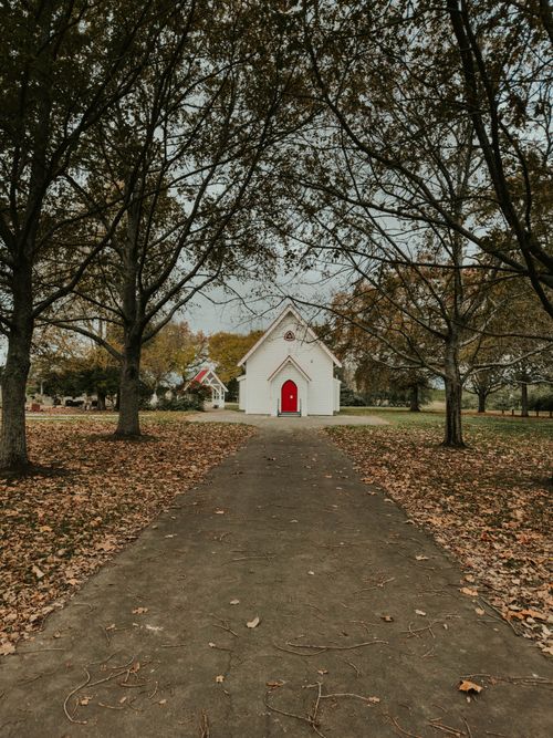 Free A quaint white chapel with a red door surrounded by autumn trees in Appleby, Tasman. Stock Photo