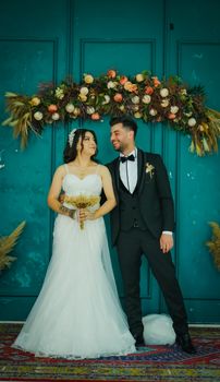 A bride and groom standing elegantly in front of floral decor at their wedding ceremony. - Fotografer Sidoarjo