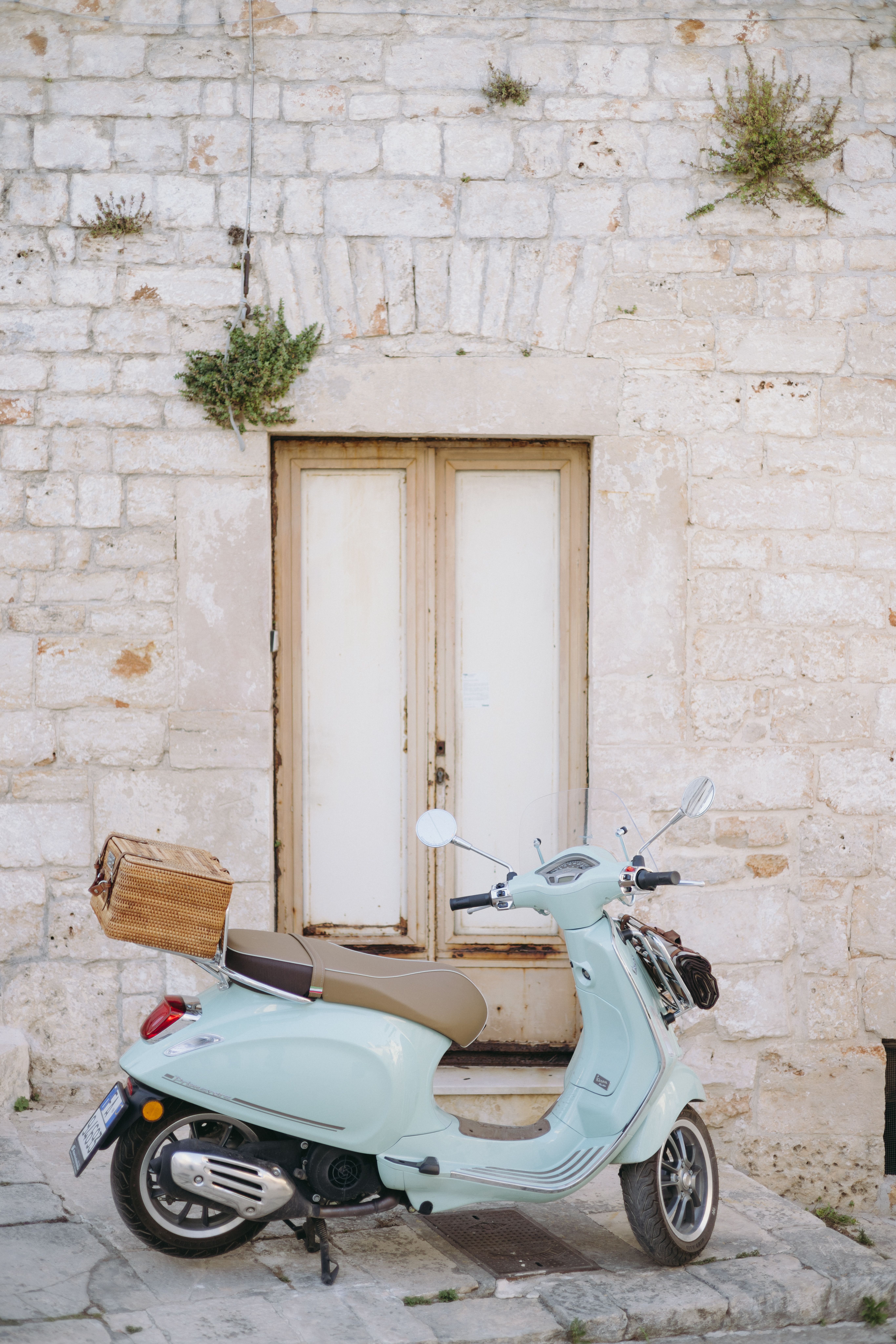 A pastel vintage scooter parked by a rustic stone wall in Alberobello, Italy.