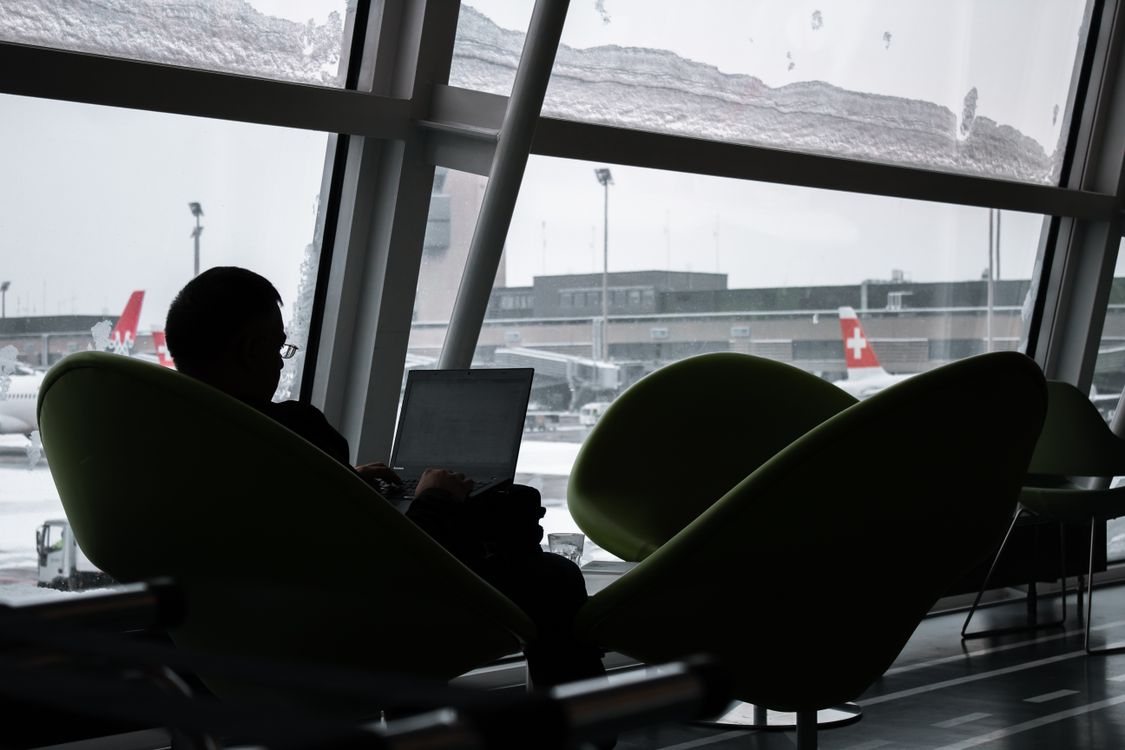 Silhouette of a man working on a laptop in an airport lounge with planes visible through the windows