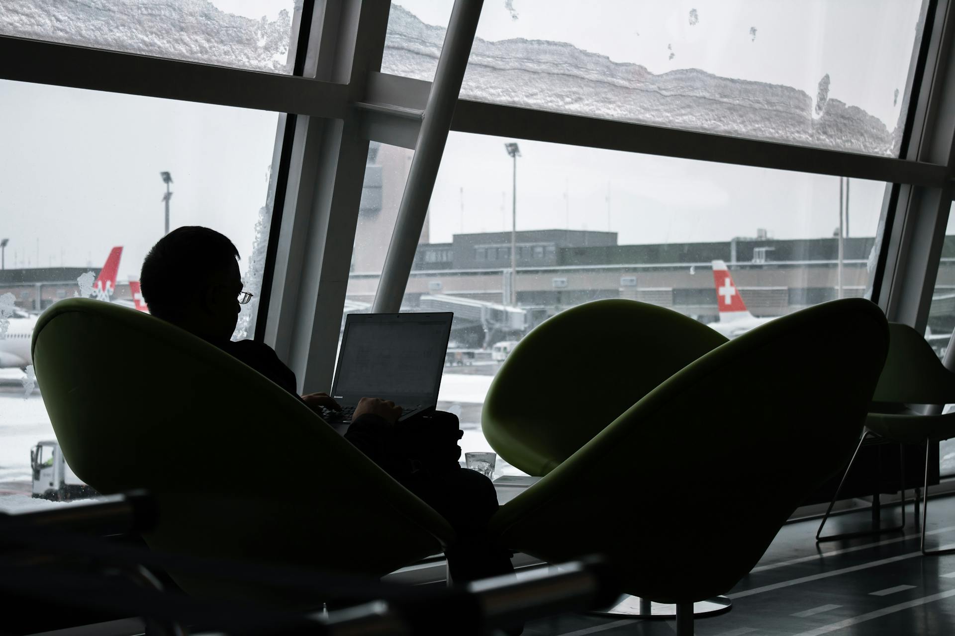 Silhouette of a man working on laptop at airport lounge with planes outside.