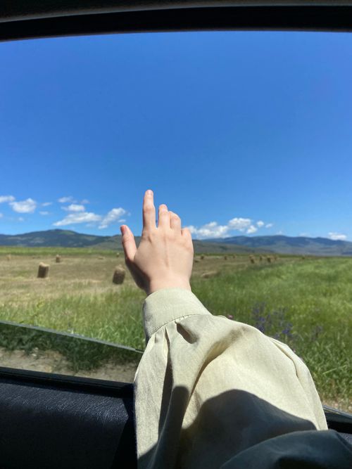 Free A hand reaching out from a car window over a lush rural countryside under a clear blue sky. Stock Photo