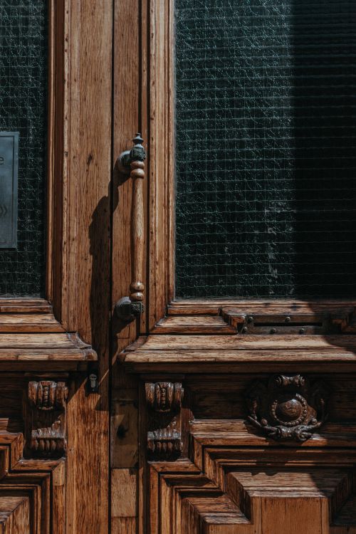 Free Close-up of a sunlit ornate wooden door featuring intricate carvings and vintage metal handle. Stock Photo