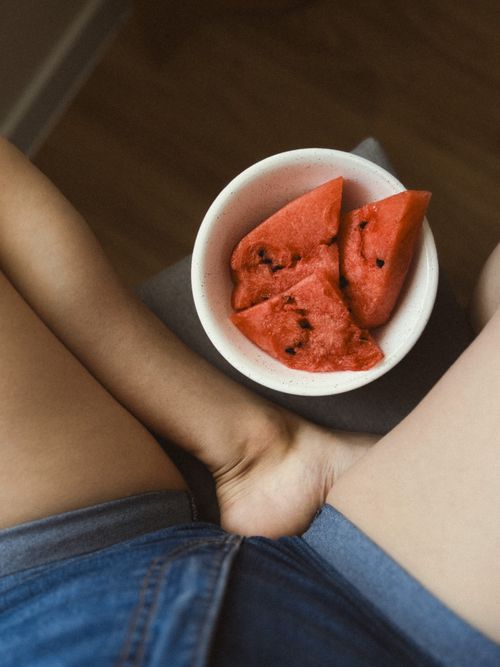 Free A close-up of a bowl with fresh sliced watermelon resting on a woman's lap in a casual setting. Stock Photo
