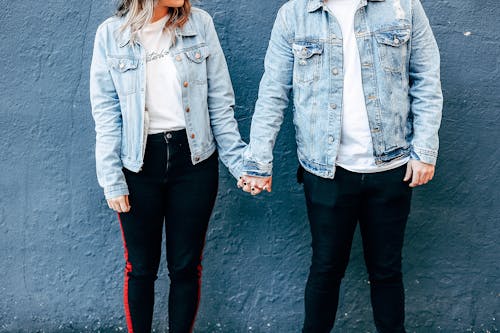 Two Person Standing and Holding Their Hands Beside Blue Wall