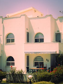 Charming white Mediterranean style house with garden and arched windows under clear sky.
