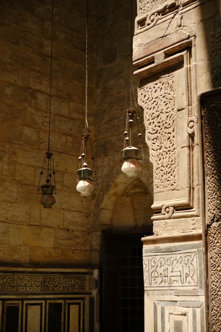 Close-up of ornate Middle Eastern stone architecture with hanging lamps.
