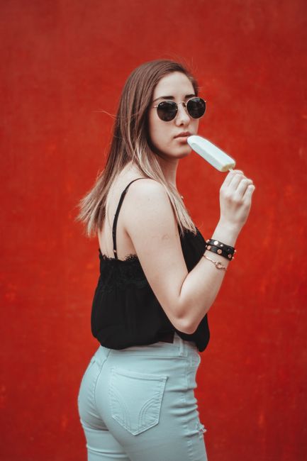 Stylish woman with sunglasses and ice cream against a vibrant red background in Mexico City.