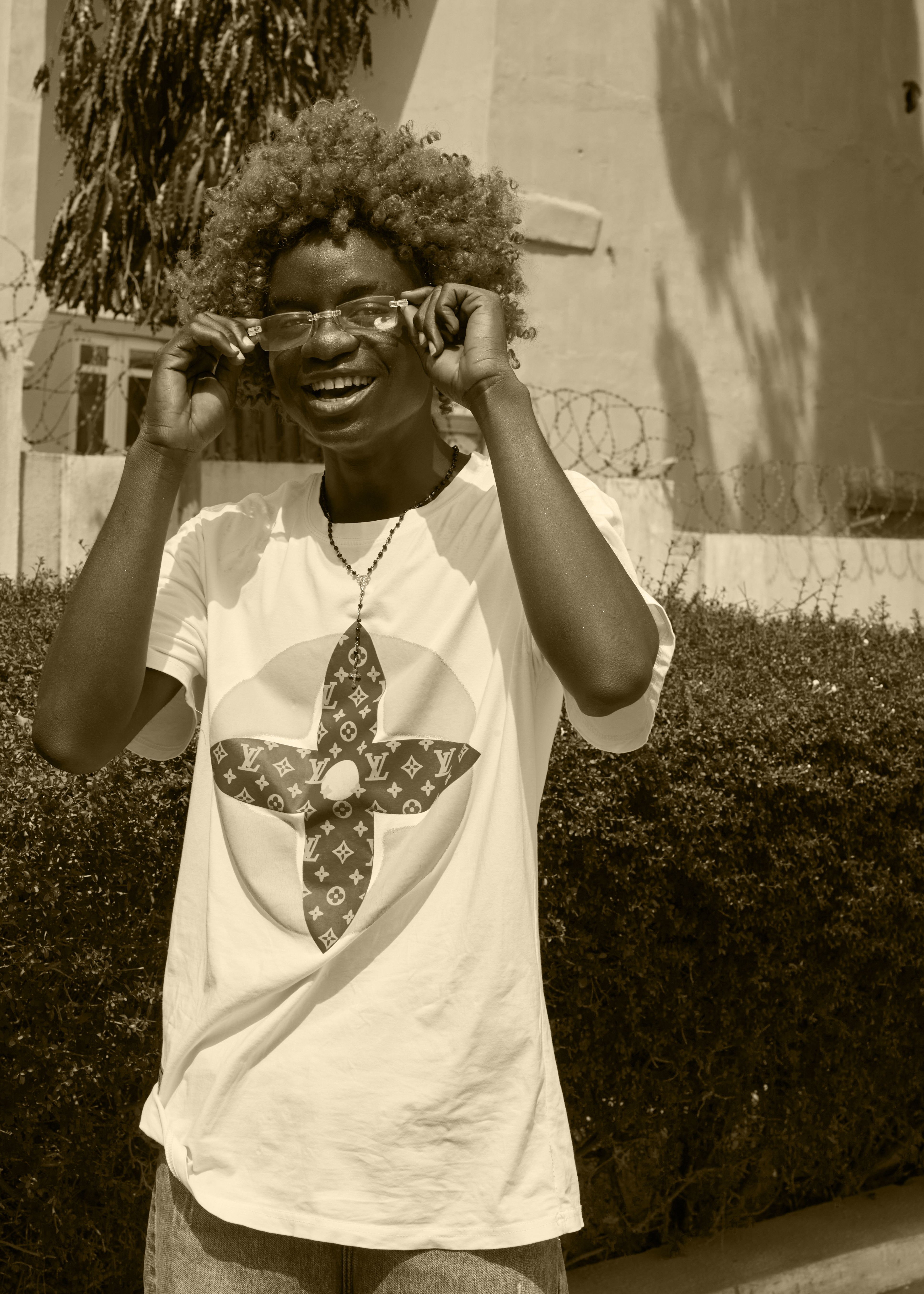 Fashionable portrait of a smiling man with curly hair and eyeglasses in a white t-shirt, outdoors.
