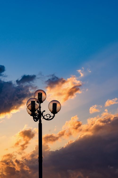 Free A street lamp silhouetted against a vibrant sunset sky with dramatic clouds. Stock Photo